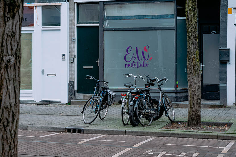 Foto van de gevel van een nagelstudio met fietsen voor de deur en afgeplakte ramen.