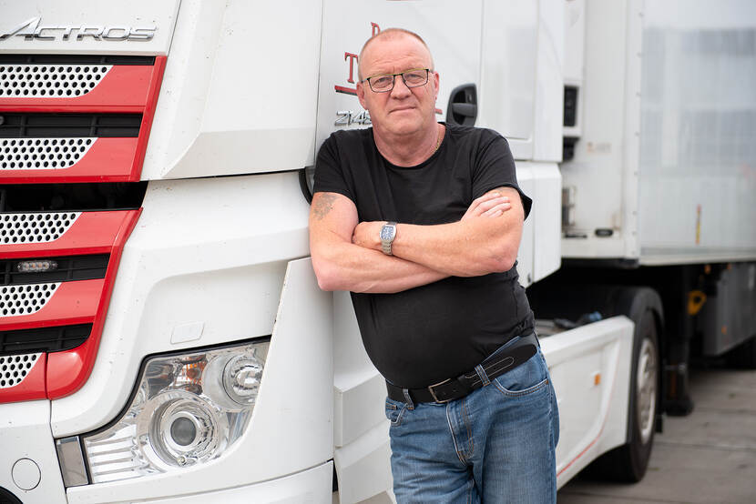 Fotoportret van vrachtwagenchauffeur Don die met zijn armen over elkaar tegen de portier van zijn vrachtwagen aanleunt.